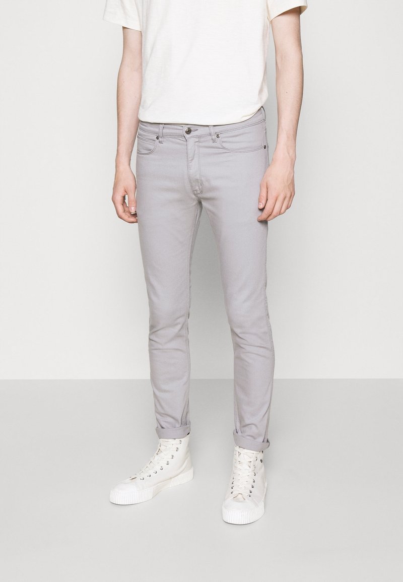 Jean slim gris clair avec cinq poches et fermeture par bouton, associé à un t-shirt crème à manches courtes et des baskets montantes blanches.