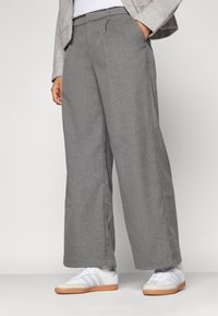 Grå vida byxor med en strukturerad yta och sidofickor, tillsammans med vita sneakers med grå ränder och en gummisula.