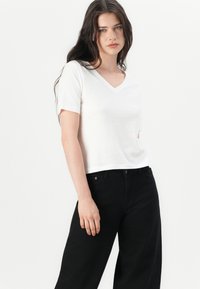 White V-neck t-shirt made of soft fabric, paired with high-waisted black jeans. Simple, relaxed-fit design with short sleeves.