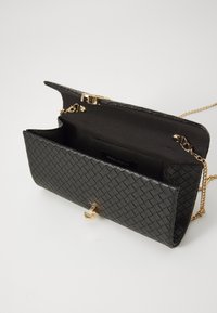 Fekete szőtt clutch táska arany kiegészítőkkel. A belsejében sötét szövet bélés és márkás címke található. Lánc pánt van hozzácsatolva.