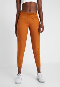Nike Sporthose in Orange, mit schmalem Schnitt, elastischem Bund und perforierten Details an den Seiten. Kombiniert mit weißen Schuhen.