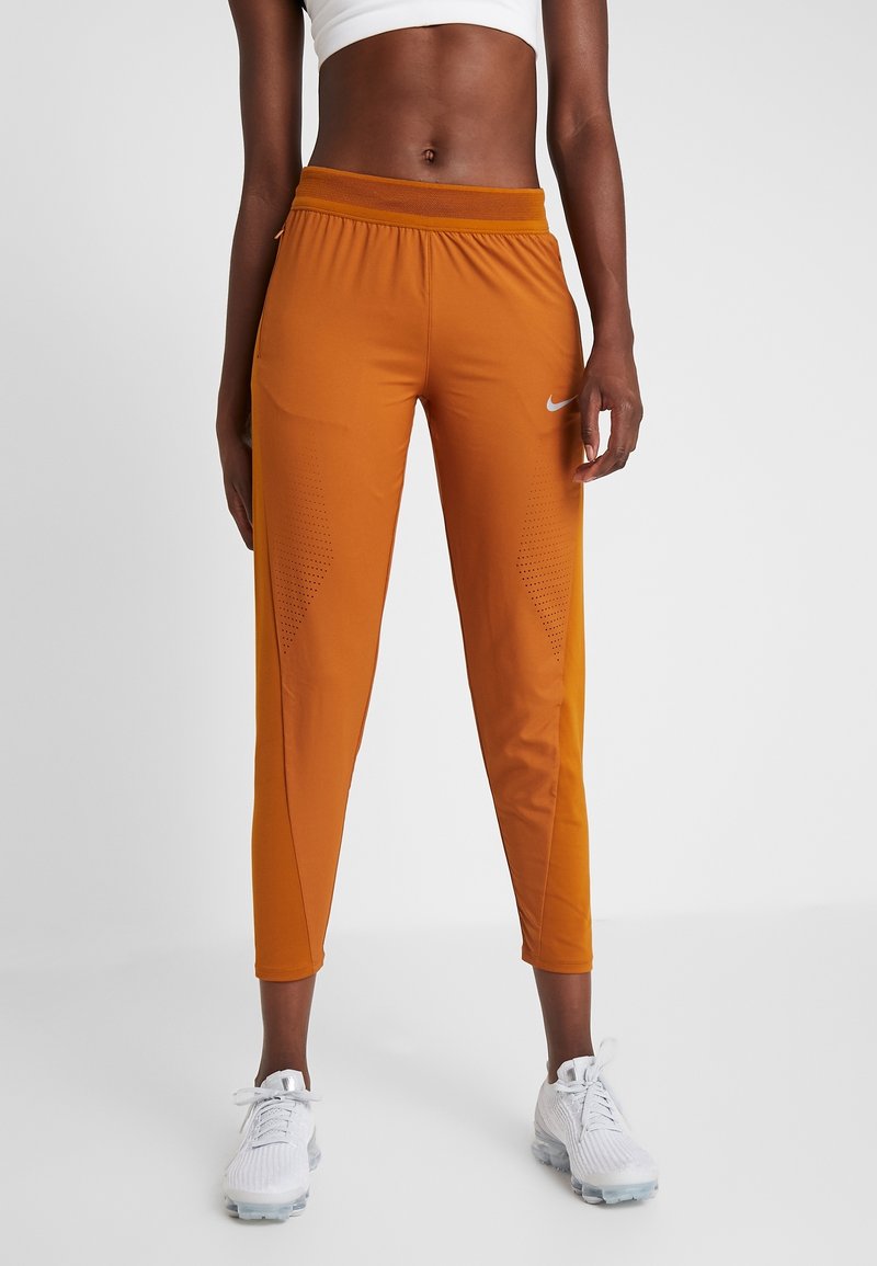 Nike Sporthose in Orange, mit schmalem Schnitt, elastischem Bund und perforierten Details an den Seiten. Kombiniert mit weißen Schuhen.