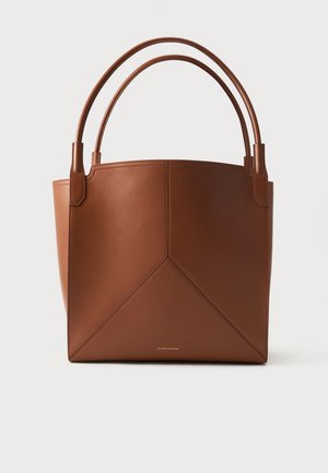 Bruine leren tote bag met dubbele handvatten en geometrisch stikseldetail tegen een effen lichte achtergrond.