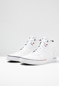 Bílé vysoké tenisky vyrobené z hladké kůže s perforacemi, kontrastními námořnickými a červenými akcenty a plochými tkaničkami. Gumová podrážka.