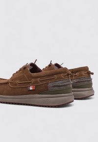 Scarpe in suede marrone con dettagli in verde oliva, pannello grigio testurizzato e rifiniture rosse. Presentano un'importante lacciatura e una suola spessa in gomma.