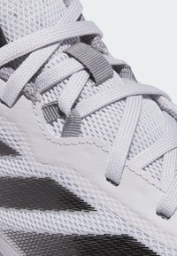 Zapatilla deportiva blanca con parte superior de malla, cordones grises y un patrón geométrico negro en el costado. Superficie texturizada con elementos de diseño flexibles.