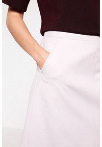Falda de mezcla de lana en rosa claro con bolsillos laterales y una cintura ajustada, exhibida junto a una blusa de color burdeos oscuro. Textura suave y líneas limpias.