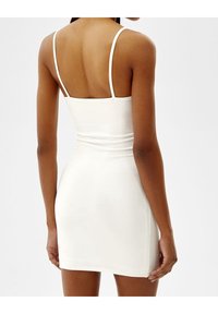 Robe mini blanche avec fines bretelles, texture côtelée et design ajusté, présentant un dos échancré et une longueur mi-cuisse.