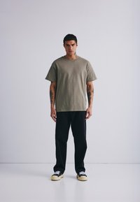 Olivengrønn kortermet skjorte med rund hals, kombinert med svarte bukser og svarte joggesko med hvite såler. Enkel design, avslappet passform.