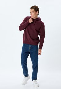 Felpa con cappuccio bordeaux con tasca a marsupio, abbinata a jeans blu larghi e sneakers bianche. Tessuto morbido con una vestibilità comoda.