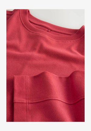 Red sweatshirt with a crew neck, featuring a textured fabric, visible stitching detail, and a slightly raised pocket section.