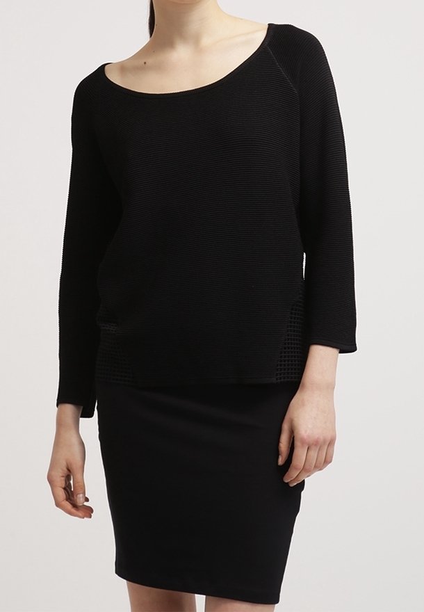 Femme portant un haut noir texturé à manches longues avec un col arrondi et une jupe noire ajustée longueur genou.