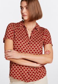 Camisa de manga corta en rojo con un estampado floral, que presenta un cuello con solapa y cierre de botones. Tejido suave con un corte relajado.