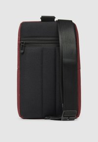 Bolso bandolera de tela texturizada roja y negra con un bolsillo con cremallera, correa ajustable y respaldo acolchado para mayor comodidad. Forma rectangular compacta.