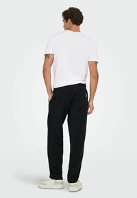 Sorte sweatpants med en afslappet pasform, elastisk talje, baglomme, kombineret med en hvid t-shirt med korte ærmer og cremede sneakers.