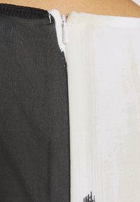 Detailní záběr na bílý zip zapínající oděv s černobílými látkovými panely proti pokožce.
