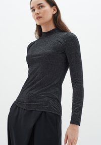 Fekete, csillogó anyagból készült, hosszú ujjú blúz, fitted szabással és magas nyakkal. Sima textúra, minimalista dizájn és látható minták nélkül.