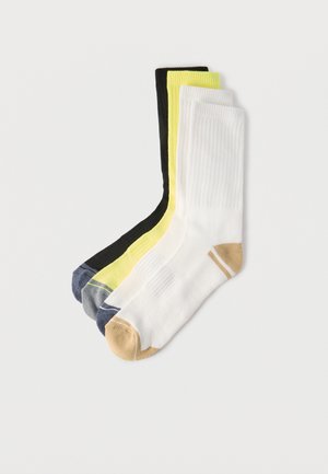 Kolm paari soonikkoes tennissukke: valged beežide varvastega, kollased hallide varvastega ja mustad siniste varvastega, üksteise kõrvale virnastatud.