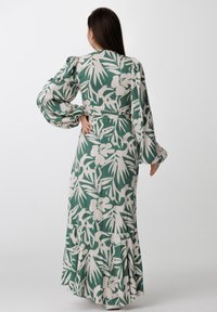 Długa zielona sukienka z białymi kwiatowymi i liściastymi wzorami. Ma bufiaste rękawy, dopasowaną talię i rozkloszowany dół z falbanami.