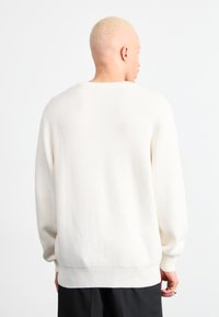 Valkoinen neulepaita, jossa on ribbireunus ja hihansuut. Sisältää klassisen pyöreän pääntien ja rennon istuvuuden, joka korostaa sileää rakennetta.