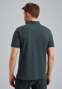 Tamnozelena polo majica od pamuka s suptilnom teksturom. Ima kratke rukave i ovratnik, s malim logotipom na leđima.