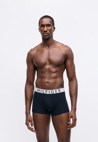 Tommy Hilfiger férfi boxeralsó fekete pamutból, fehér márkázott derékszíjjal. Rövidre vágott dizájn sima felülettel.