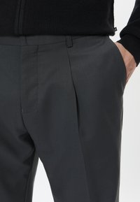 Ušité šedé kalhoty mají jemnou strukturu, elegantní design a standardní pas s bočními kapsami, což jim propůjčuje upravený vzhled.