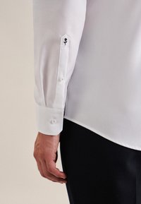 Witte dress shirt met lange mouwen, voorzien van een puntige manchetknoop en zwarte rozenborduursel bij de knoop. Glad stof met een getailleerde pasvorm.