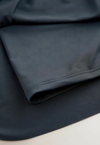 Dunkelblauer Stoff mit glatter Textur, der eine gefaltete Kante und subtile Nähedetails aufweist. Einfarbig ohne sichtbare Muster.