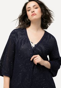 Cárdigan de punto marino con escote en V y mangas de tres cuartos, que presenta un patrón texturizado y sutiles lentejuelas en toda su superficie.