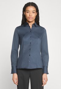 Camicetta a maniche lunghe di colore blu navy con design aderente, chiusura frontale con bottoni e texture morbida. Presenta un colletto classico e polsini con bottoni.
