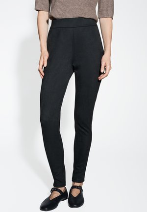 Black stretchy leggings with a high waist design. Smooth texture with no visible fastenings. Paired with black flat shoes and a brown sweater.