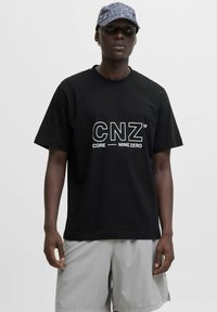 Sort bomulds t-shirt med fed hvid "CNZ" logo og "CORE NINE ZERO" tekst. Korte ærmer, afslappet pasform, parret med lysegrå shorts.