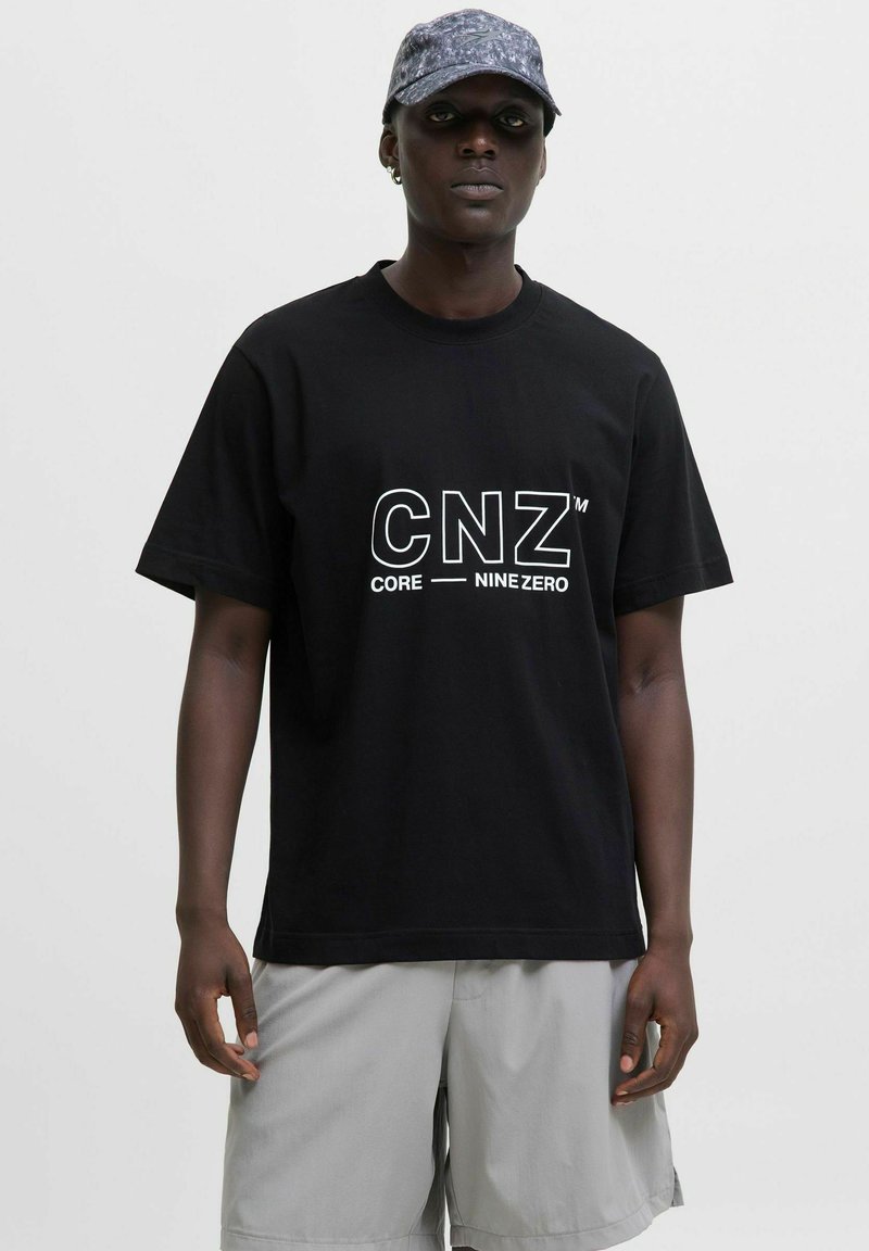 Black cotton t-shirt featuring bold white "CNZ" logo with "CORE NINE ZERO" text. Short sleeves, relaxed fit, paired with light grey shorts.
