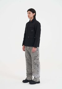 Czarna kurtka z dwoma przednimi kieszeniami, w połączeniu z jasnoszarymi spodniami cargo z misternym białym haftem i luźnym krojem. Czarne obuwie.