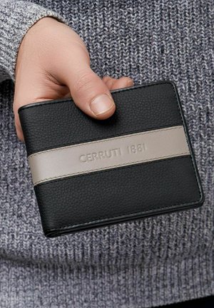 Roka drži črno denarnico z vodoravno sivo črto, na kateri je vtisnjen napis "Cerruti 1881", na ozadju sive pletene majice.