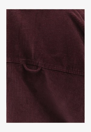 Burgundin konaaihottu kangas, jossa on pystyribbaus. Sisältää pienen silmukkatehtävän yläosassa lähellä taitettavaa saumaa.