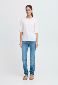 Vit kortärmad topp med rund halsringning, kombinerad med ljusblå denimjeans och tan flip-flop sandaler. Enkelt design och passform.