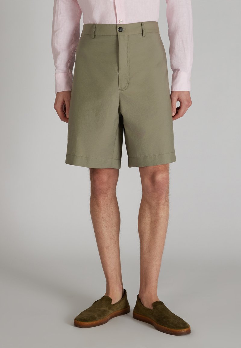 Szorty w kolorze oliwkowym z mieszanki bawełny, o prostym kroju, z zamknięciem na guzik, bocznymi kieszeniami i podwiniętymi brzegami, w połączeniu z ciemnooliwkowymi butami wsuwanymi.