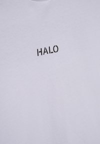 Bílá bavlněná trička s černě tištěným logem "HALO". Tkanina se zdá být hladká, má klasický kulatý výstřih a krátké rukávy.