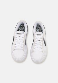 White sneakers with black accents, textured rubber sole, and flat laces. Interior features a geometric patterned lining. Clean, classic design.