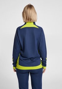 Chaqueta deportiva de la marina con acentos en verde lima, cuello alto y detalle texturizado en las mangas. Hecha de un tejido transpirable, con un diseño ajustado.