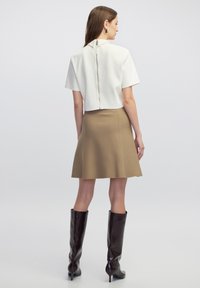 Top blanco de manga corta con cremallera en la espalda, combinado con una falda acampanada beige y botas de caña alta marrón oscuro. Texturas suaves en todo.