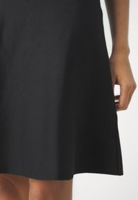 Schwarzes A-Linien-Kleid aus einem strukturierten Stoff, mit einem leicht ausgestellten Saum und sichtbarem Seitennähten.