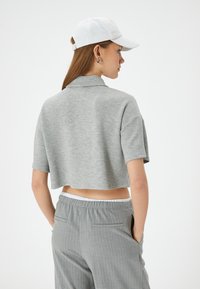 Grå kortærmet polo shirt i blødt materiale, parret med lysegrå stribede bukser, set bagfra. Hvid kasket på.