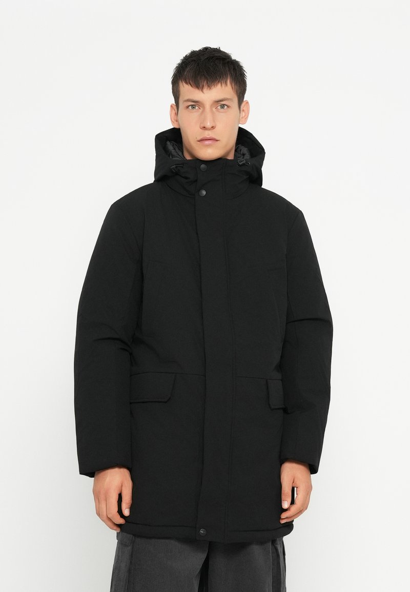Zwarte geïsoleerde parka-jas met een capuchon, een drukknoopsluiting aan de voorkant en twee zichtbare zijzakken. Gladde textuur en lange mouwen.