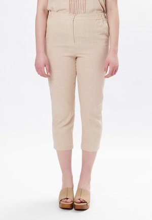 Pantalons capri beiges en tissu texturé, avec une taille élastique et un bouton unique. Associés à des chaussures à plateforme ouvertes.