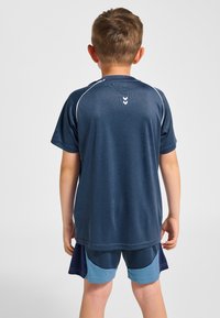 Marinblå sporttröja med korta ärmar och vita detaljer, kombinerad med ljusblå shorts med mörkblå paneler och slät textur.