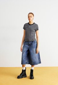 Ριγέ μαύρη και λευκή μπλούζα συνδυασμένη με φαρδιά μπλε τζιν κολάν, συμπληρωμένη από μαύρα μποτάκια με κορδόνια και λευκές κάλτσες.