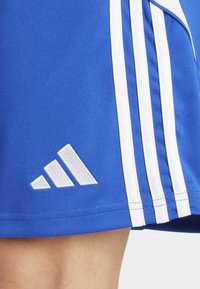 Plave sportske šortse od glatke tkanine, s tri vertikalne bijele pruge i bijelim Adidas logotipom na rubu.